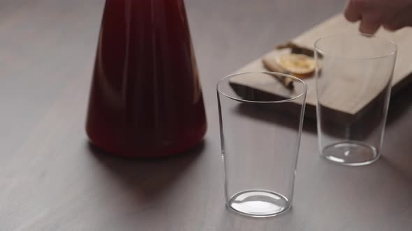 Slow Motion Man Hand Serving Mulled Wine in Thin Tumbler Glasses on Walnut Table