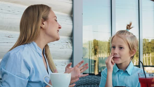 In a Cafe and on Wicker Chairs a Woman and a Boy with Blond Hair with Hangings are Resting