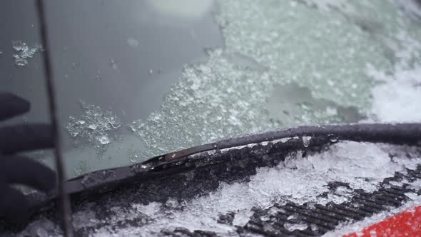 Man cleaning and scraping ice from car windshield wipers in snow