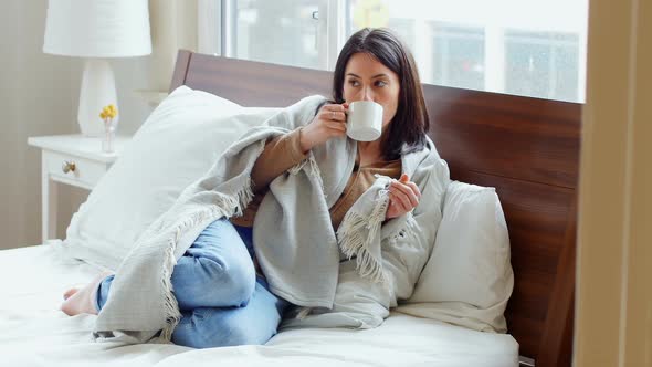 Thoughtful woman wrapped in blanket having coffee 4k