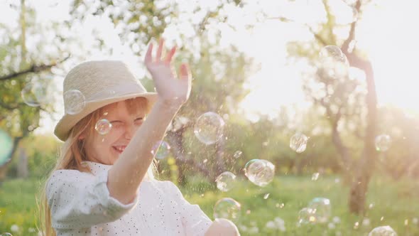 A Cheerful Girl in a Hat Carelessly Plays with Soap Bubbles. Happy Spring and Good Weather