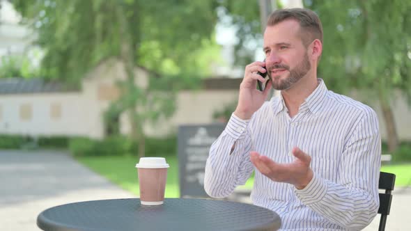 Middle Aged Man Talking on Smartphone in Outdoor Cafe