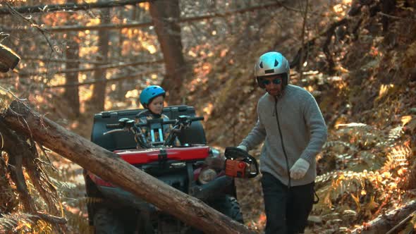 An Autumn Forest - Man Takes a Chainsaw and His Son Is Waiting for Him on a Quad Bike