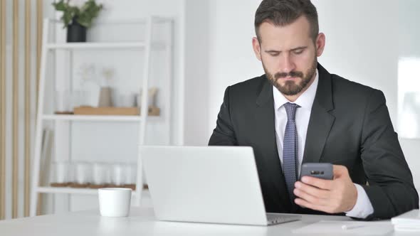 Businessman Using Smartphone and Laptop at Work