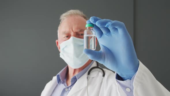 Portrait of caucasian senior male doctor wearing face mask holding covid-19 vaccine