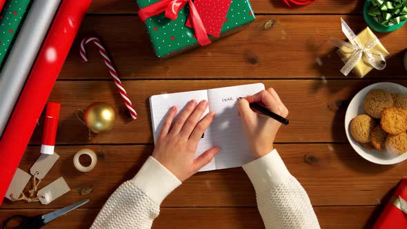 Female's Hands Writing Letter To Santa in Notebook