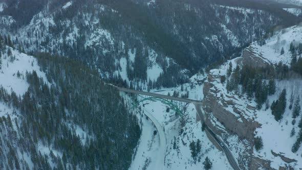 Aerial Drone Shot Flying Over Scenic Green Bridge Over Snowy Mountain Valley