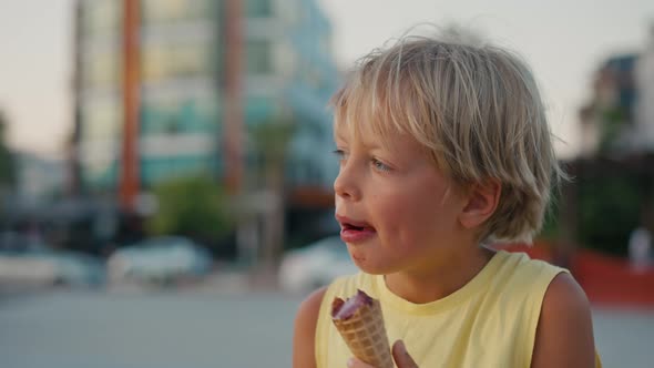 Outdoor Portrait of Young Caucasian Boy with Blond Hair Eating Ice Cream in Crispy Cone