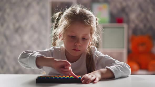 Little Kid with Blonde Plaits Touches Abacus By Finger