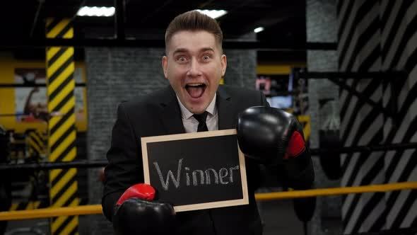 A Businessman in a Boxing Gloves Holds a Board with the Inscription WINNER