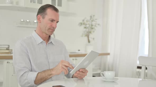 Excited Middle Aged Man Having Success on Tablet at Home