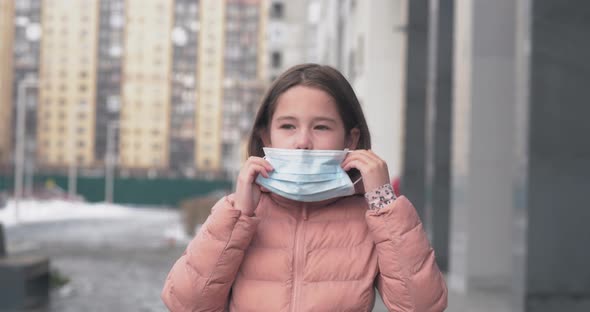 Coronavirus Protection. A Caucasian Girl Puts on a Medical Protective Mask Standing on a Street