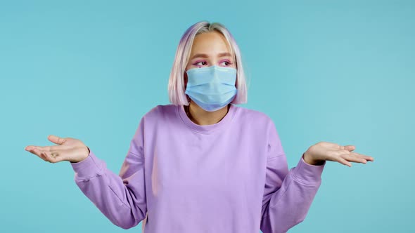 Young Pretty Unsure Woman in Protective Mask Shrugs Arms, Makes Gesture of I Don't Know, Can't Help