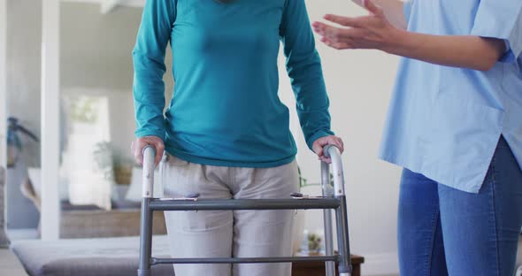 Female health worker assisting senior woman to walk with walking frame at home