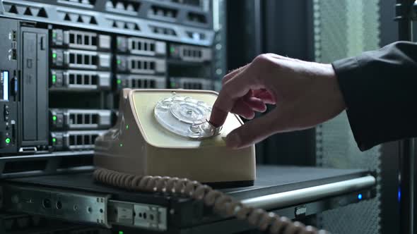 man calls on a dial phone, which stands against background of a server cabinet