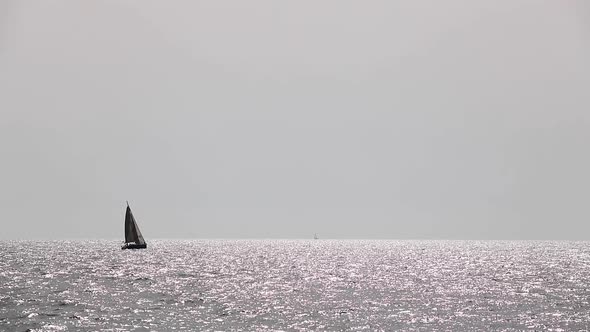 A sports yacht and a windsurfer sail the Mediterranean during the day.