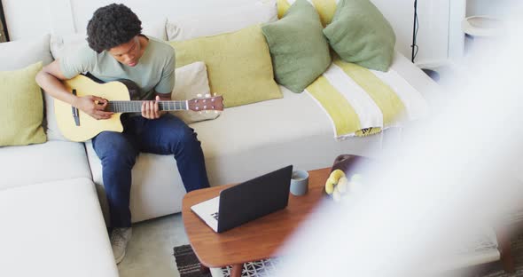 African american man plays guitar and singing, using laptop at home