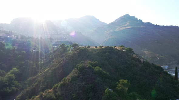 Beautiful aerial shot with sunset over green mountains; sun-covered. Landscape; camera goes down.