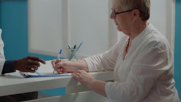 Close Up of Elder Patient Signing Checkup Documents