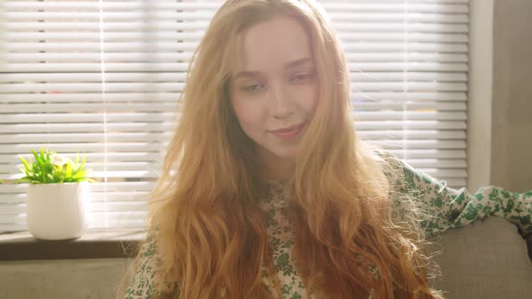 Young Beautiful Redhaired Woman Relaxes on the Sofa Near the Window in the Living Room