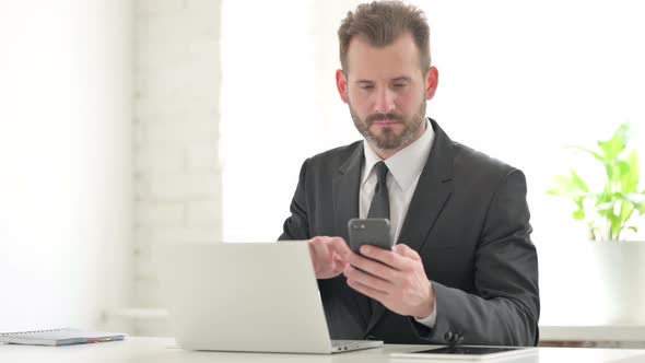 Young Businessman Using Smartphone While Using Laptop in Office