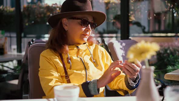 A Mature Adult Woman Drinking Coffee and Using Her Smartphone at the Cafe