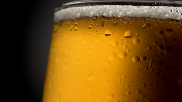 Beer Mug Close-up. Wet, Rotating Glass Filled with Golden-colored Cooled, Foamy Beverage on a Dark