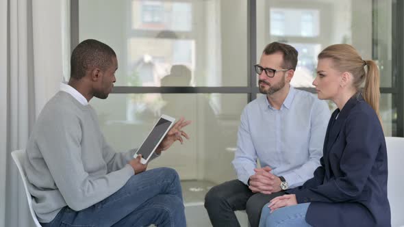 African Businessman with Tablet Interviewing Businessman and Young Businesswoman