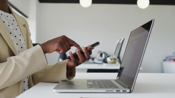 Close up of hands of african american businesswoman sitting at desk using smartphone