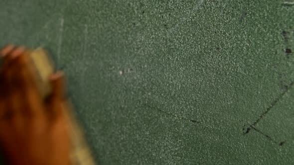 Hand of schoolboy rubbing chalkboard with duster in classroom