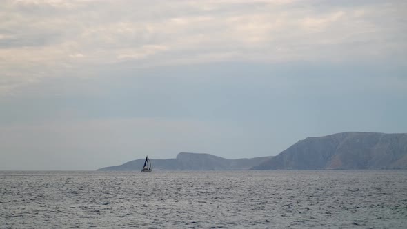 Sail Yacht Cruising on Deep Blue Sea Water Over Overcast Sky