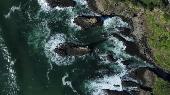 High view of waves breaking over a towering volcanic rock ledge on a coastal headland. Drone view