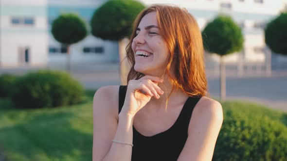 Portrait of Beautiful Smiling Redhaired Woman on Street at Sunset