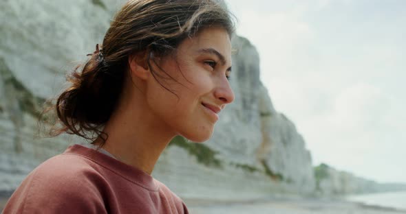 A Young Beautiful Woman Sits on the Seashore Next to Limestone Cliffs