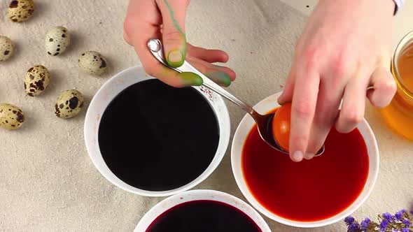 Caucasian Child Paints Easter Eggs with a Metal Spoon Dipped Into a White Bowl with Dye