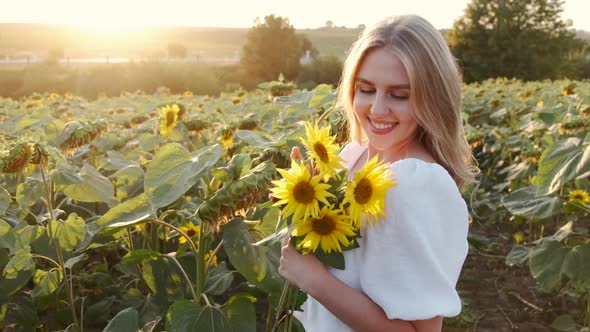 Girl Smells Bouquet of Sunflowers in the Field in Sunrays