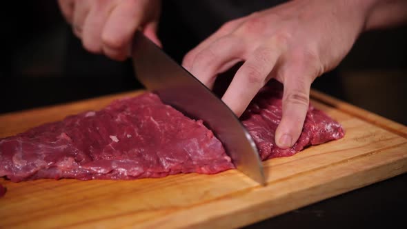 chef cuts raw meat with a kitchen knife on a wooden board