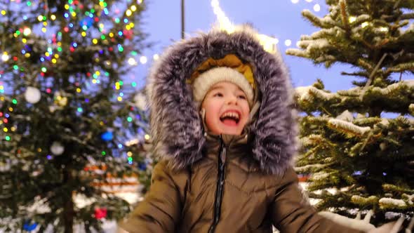 Portrait of happy girl in winter in fur hood against background of fairy lights, Christmas trees