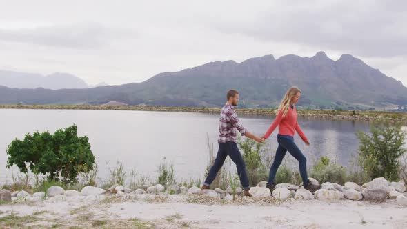 Caucasian couple having a good time on a trip to the mountains, walking near lake and holding hands