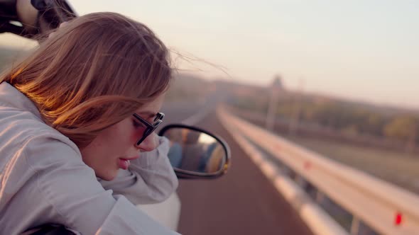 A Young, Beautiful Woman Relaxes and Enjoys a Road Trip in the Front Seat of a Cabriolet Car with