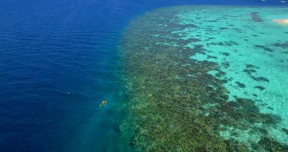 Aerial drone view of a man and woman couple snorkeling over a coral reef of a tropical island.