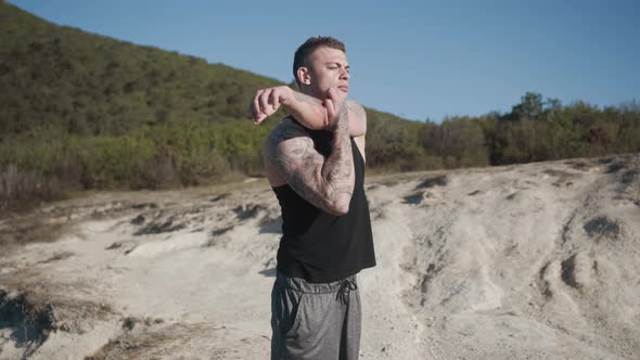 Tattooed Muscular Man Does Workout Outdoors at Sunny Day, Greenery on Background