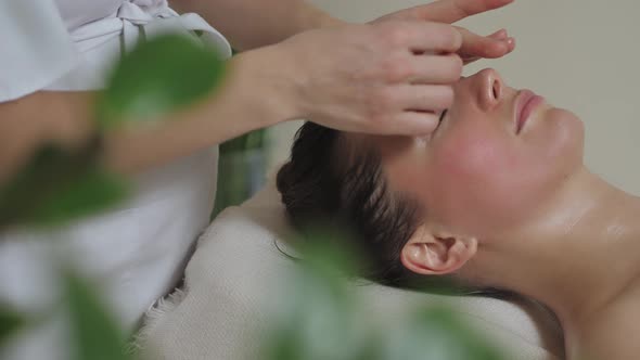 Beautiful Brunette Woman Lies on a Face Massage with Gouache Stones