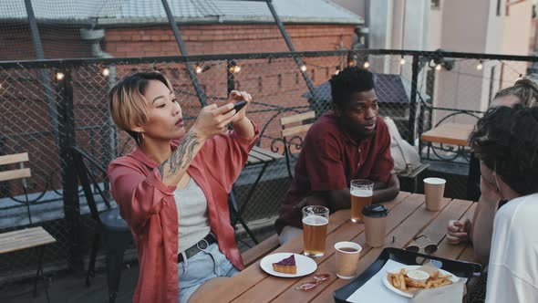 Asian Woman Taking Photo of Food on Table at Rooftop Bar