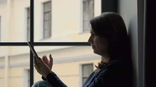 Woman Uses Smartphone While Sits on Windowsill