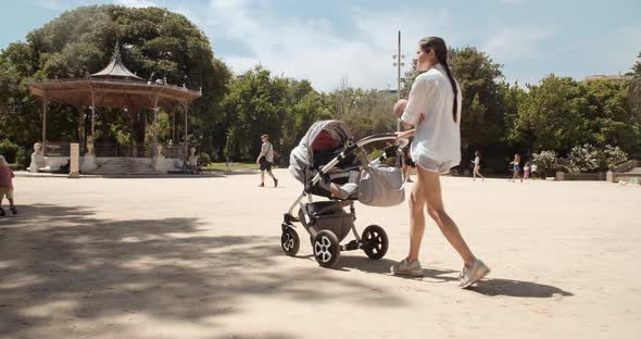 Young Mother Walking Trough Park in Tourist City Barcelona with Baby on Hands