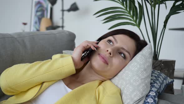 Young Woman Talking on Phone While Laying on Sofa at Home