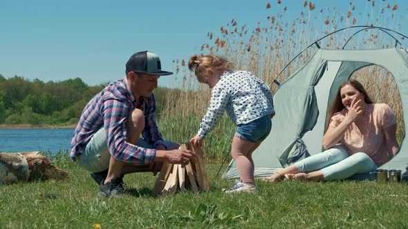 Family is Resting on the Bank of the River with a Tent