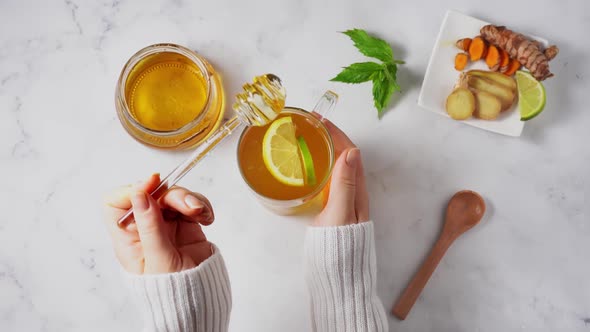 Female Hands with White Sweater Holding a Glass Cup of Anti-inflamatory Turmeric Ginger Tea