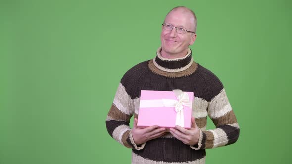 Happy Mature Bald Man Thinking While Holding Gift Box